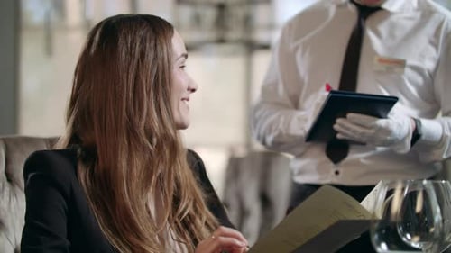 Smiling Woman Talking with Waiter in Restaurant. Happy Woman Reading Menu In