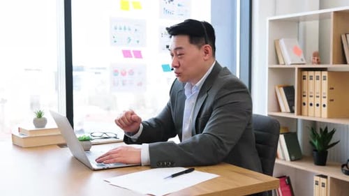 Asian Businessman Using Laptop for Video Call in Modern Office