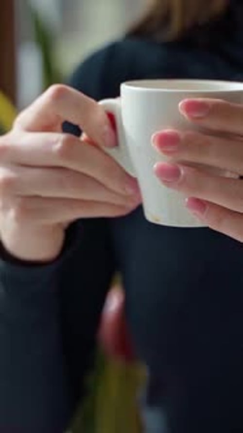 White cup with coffee in woman's hands. Beautiful young woman enjoying hot drink in a cafe.