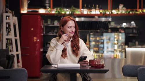Woman Sitting at Table Using Phone and Pen