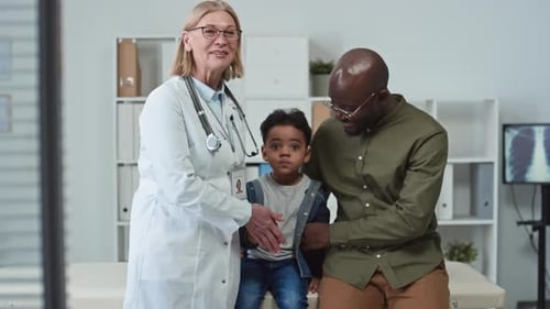 Happy Young Man with His Son and Mature Doctor Looking at Camera in Clinics