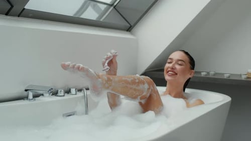 Attractive Woman Shaving Legs in Bubble Bath, Smiling