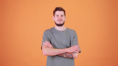 A Young Man with a Tattoo on His Arm Stands Against an Orange Background Smiling Warmly at the