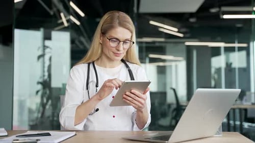 A woman doctor in a white coat is using browsing digital tablet in modern hospital clinic. Female