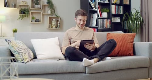 Young Man Relaxing on Sofa with Tablet