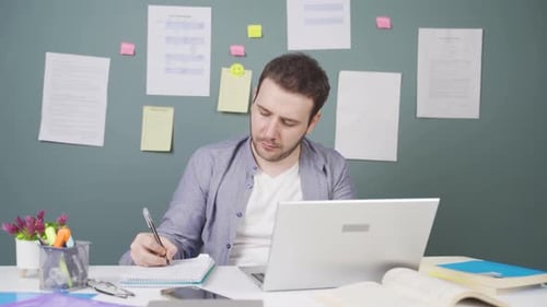 Man Using Laptop and Notebook at Desk