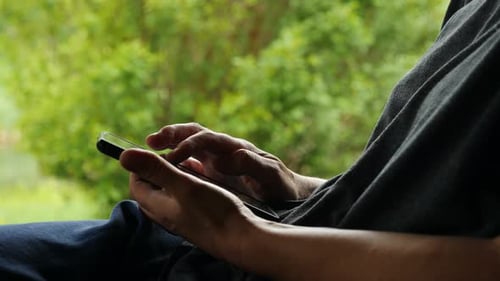 Person Typing and Scrolling on Mobile Phone with Lush Green View