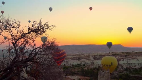 Hot air balloons burning fuel fly over city of Goreme with sightseeing tourists