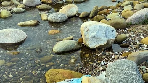 Plastic Waste Revealed Among Rocks in Shallow Riverbed Close-Up