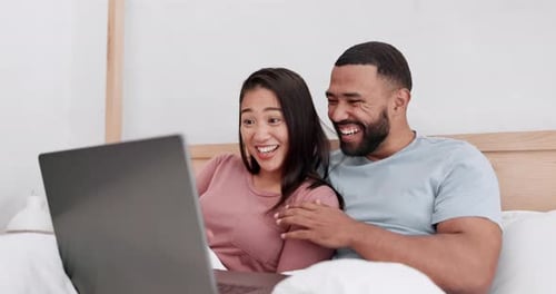 Laughing Couple Relaxing with Laptop in Bed