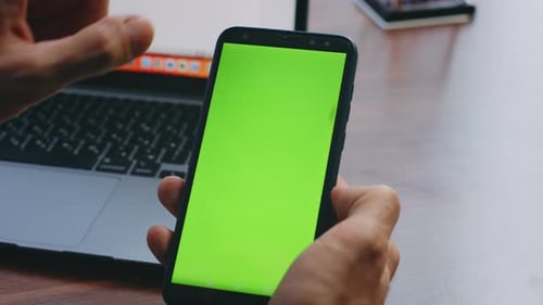 Man Fingers Scrolling Green Screen Smartphone Sitting Desk with Laptop Close Up