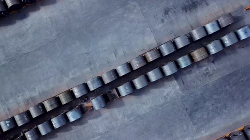 Symmetrical rows of manufactured steel rolls stored outside aerial top down view