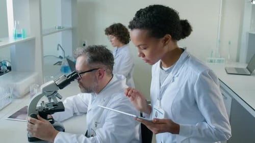 Scientists Using Microscope and Tablet in Lab