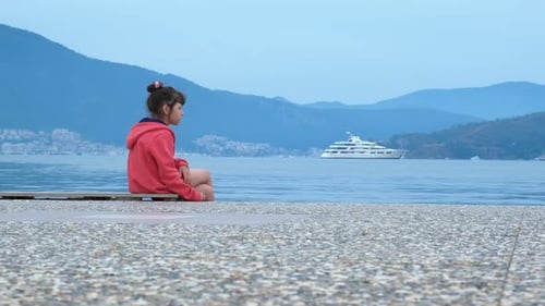 Girl Sits By Water With Yacht Background