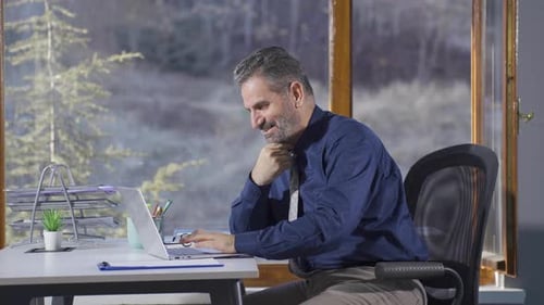 Mature Man Celebrating Success at Desk with Laptop