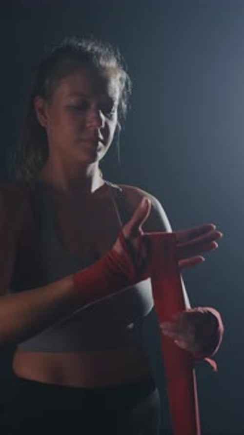 Una boxeadora femenina se da la mano para entrenar en un gimnasio con poca luz