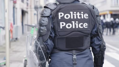 Un policier belge en tenue anti-émeute debout dans une rue urbaine en attente d'ordres