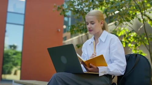 Young Woman Studying Outdoors with Laptop and Notebook