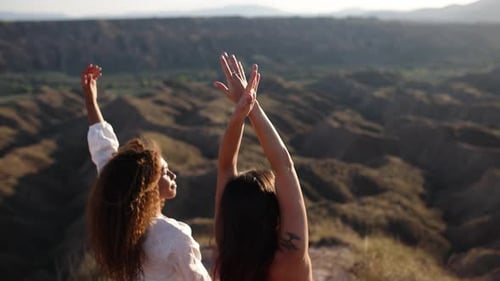 Two Dancers Raising Arms on Mountain Top at Sunset