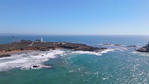 An Aerial View of a Coastal Lighthouse Standing Tall Amidst a Rocky Shoreline on a Clear Sunny Day