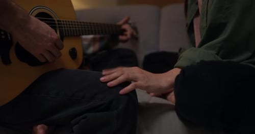 Close Up of a Guy Playing Guitar for His Girlfriend Who is Clapping Her Knees to the Rhythm While