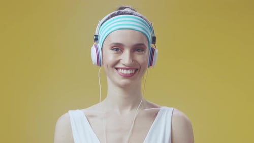 Smiling Woman with Headphones Gesturing on Yellow Background