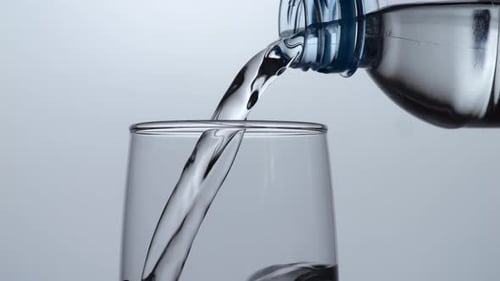 Close Up Of Drinking Water In A Bottle Being Poured Into A Glass On The Light White Background