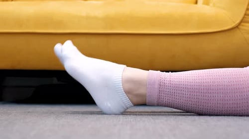 Female legs in socks bend and unbend feet against the background of yellow sofa.