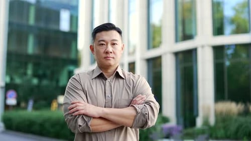 Portrait of a confident asian businessman in a shirt standing on the street near office building.