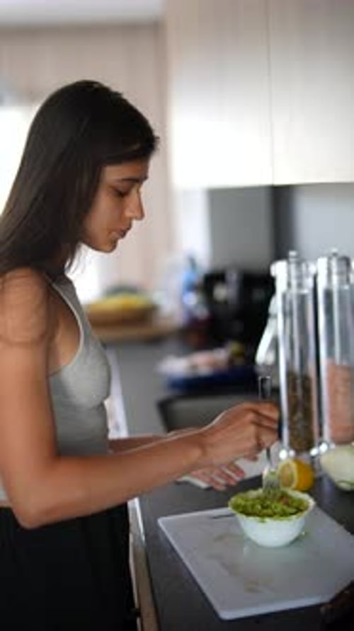 Woman Prepares and Tastes Food in Bright Kitchen