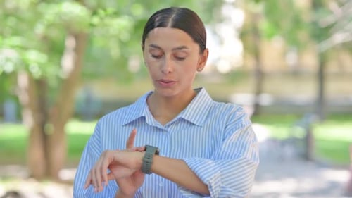 Woman Checking Smart Watch in City Park on Sunny Day