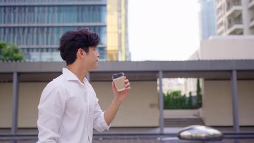 Asian young businessman drinking a cup of coffee while walking in city.