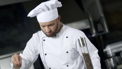 Male Chef Sprinkles Salt in Commercial Kitchen