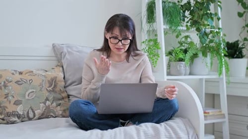 Frau mittleren Alters sitzt zu Hause auf der Couch und benutzt Laptop für Videoanrufkonferenz