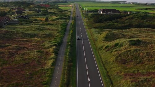 Aerial View of Cars Driving Along a Road Surrounded By Grassy Dunes and Houses with the Ringkobing