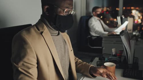 Employé noir masqué de l'entreprise travaillant de nuit et s'étirant