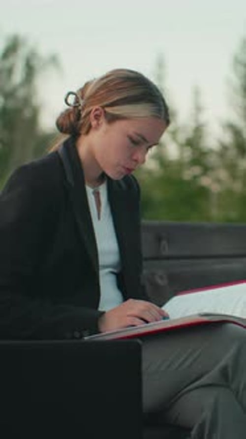 Lady Reading Book Alone Outdoors with Laptop in Quiet Urban Park Setting
