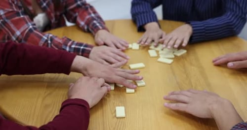 Friends playing dominoes at wooden table indoors, closeup
