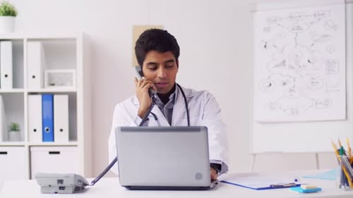 Indian doctor at hospital working with laptop and phone in healthcare job