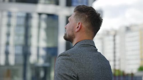Back View of the Thoughtful Businessman Wearing in a Formal Suit Standing Outside Near a Modern