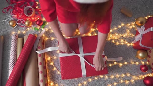 Woman Tying Ribbon on Christmas Present at Home