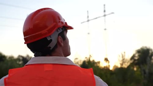 Young Engineer Standing Outdoors While Looking at the High Voltage Power Lines Back View Energy