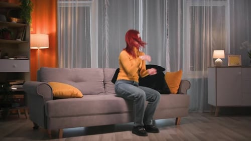Redhead Tired Woman in Outerwear Walks Up and Falls on the Sofa Takes Off Her Boots Throwing Them