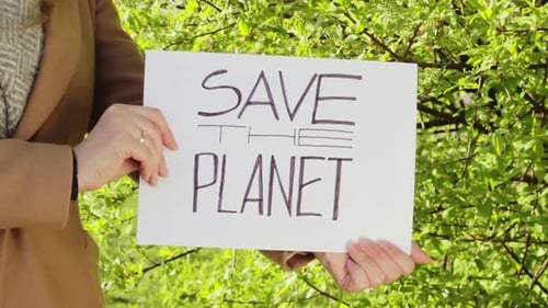 Woman hold SAVE THE PLANET board with green vibrant tree in background