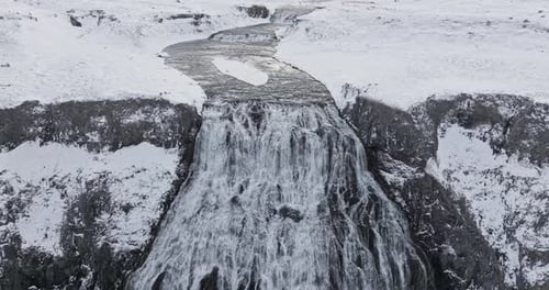 Wide Waterfall Cascading In Between Snowy Cliffs