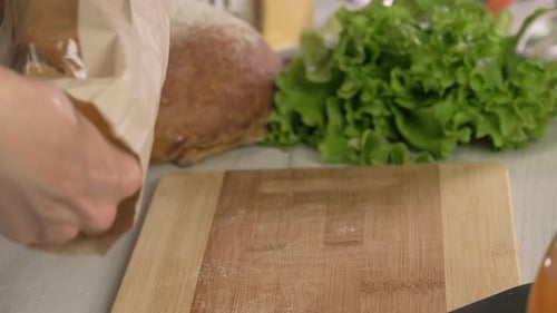 Hands of young woman european puts freshly baked loaf of baguette on cutting board, left side clos