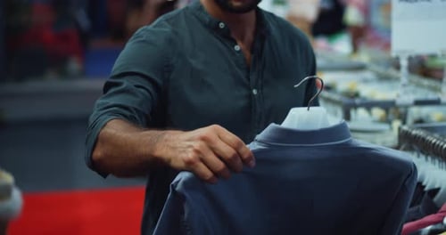Foco seletivo na mão de um belo jovem comprador inspecionando uma camisa casual pendurada em um