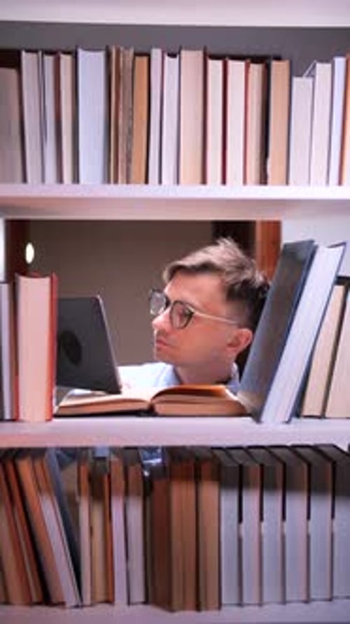 Vertical Video Student Reading Tablet and Books Between Shelves in Library at Night