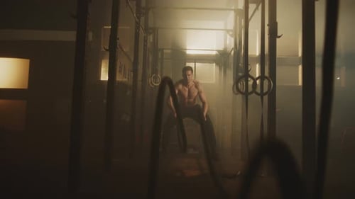 Muscular Man Working Out with Battle Ropes in Gym