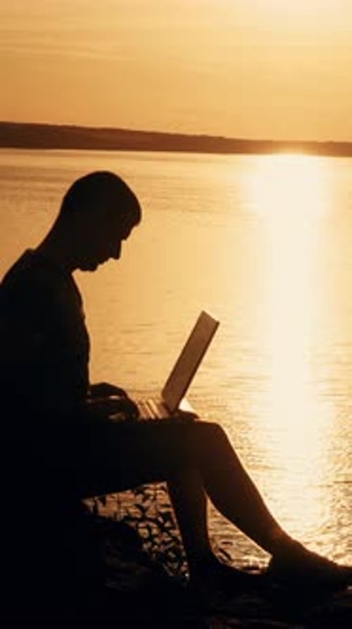 man sit and work on the laptop by sunset (sunrise) background on the top of the hill. Vertical video